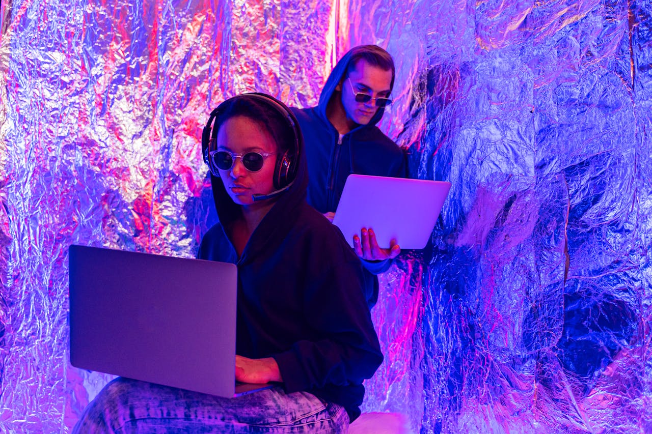 2 Women Sitting on Purple Floral Textile Using Macbook